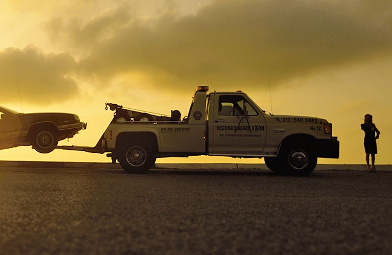 A woman stranded by the side of the road stand beside a tow truck