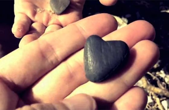 An outstretched hand holding a small rock shaped like a heart