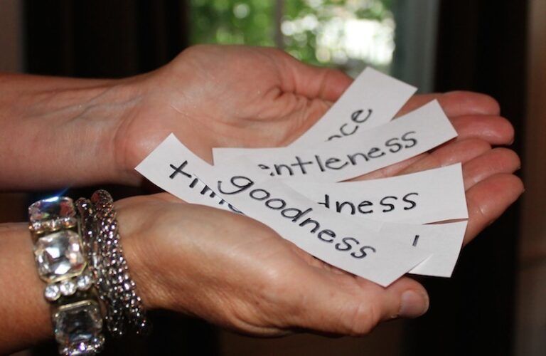 Outstretched hands hold slips of paper that read Goodness, Kindess, etc.