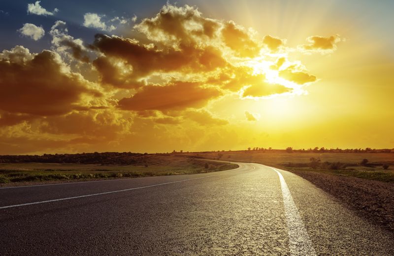 Heavenly beams shine down through the clouds on a curving highway.