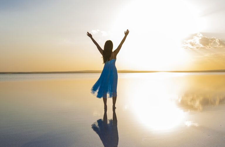 A photograph of a woman lifting her hands while standing on the beach