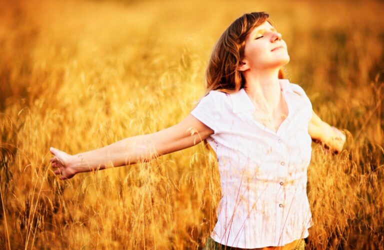 woman with arms outstretched in a field of wheat.