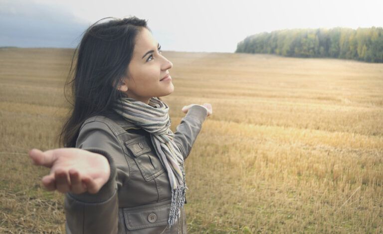 A woman in a field lifts her arms in surrender