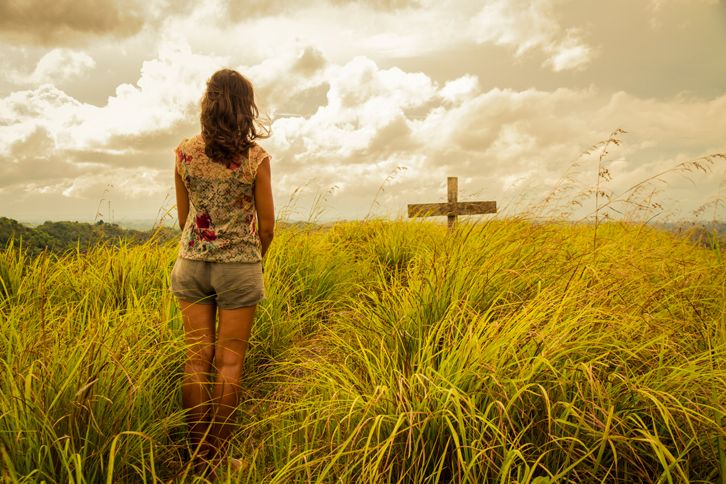 A woman in a field with a cross in front of her