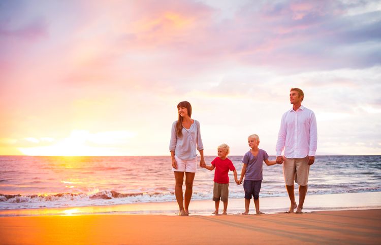 A family of four strolls the beach as the summer sun sets on the horizon.