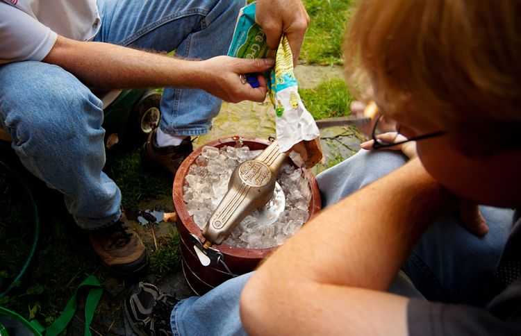 Two men hunch over a hand-cranked ice cream maker, adding rock salt to the ice.