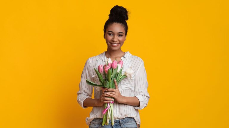 Woman on a yellow background holds pink tulips and listens to spring quotes