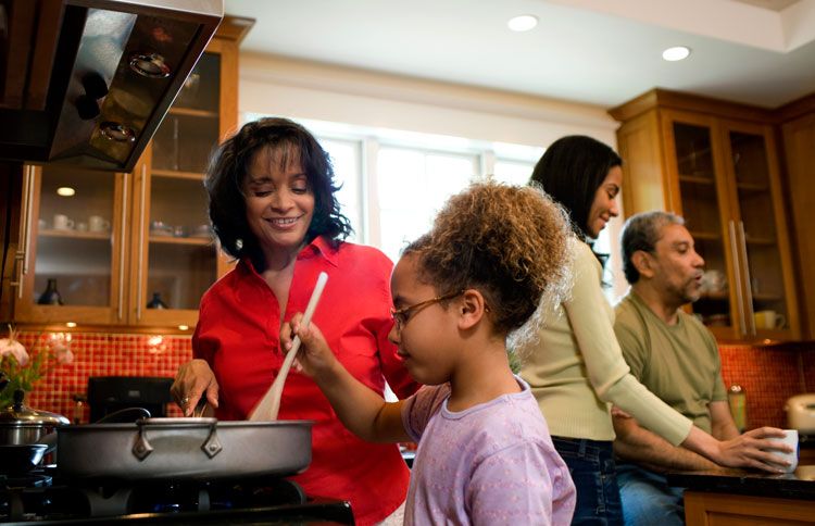 A young girl stirs the pot while her mother instructs her