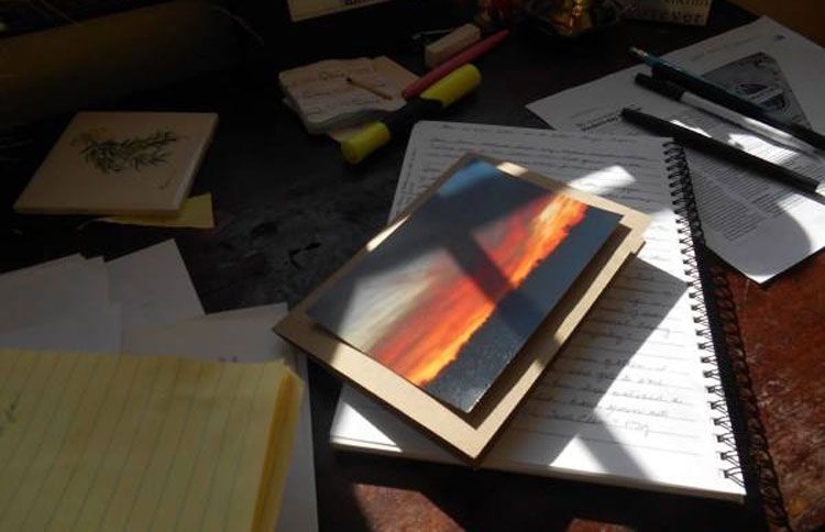 A cross against a condolence card's image of a beautiful, prairie sunset