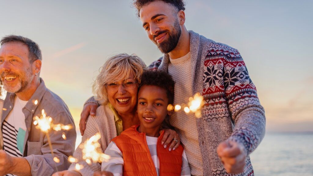 A family with sparklers on the beach saying a new year prayer for family