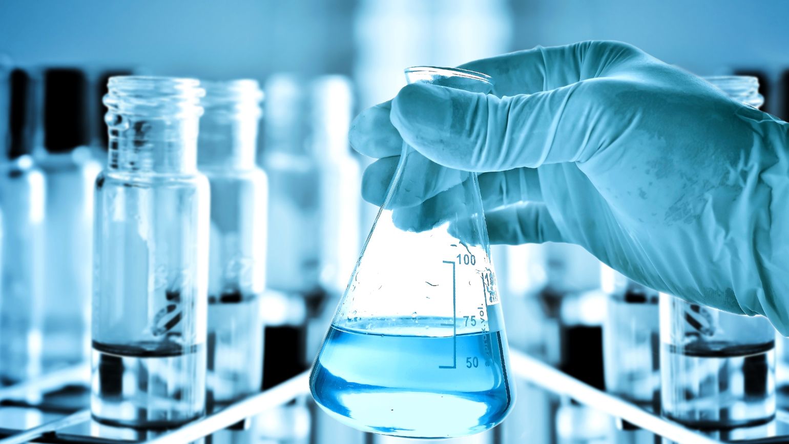 Gloved hands with a safety glass flask in a laboratory.