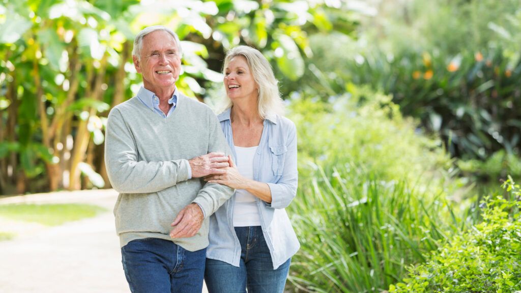 An older couple walking through a lush, green, scenic park.