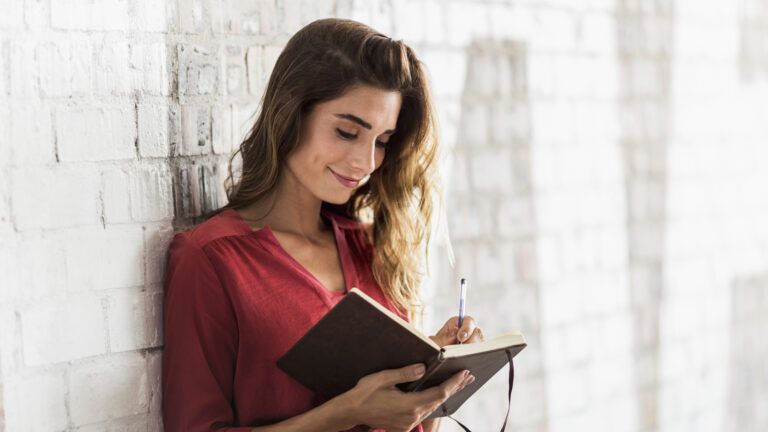 A smiling woman writing her New Year's resolutions in a journal