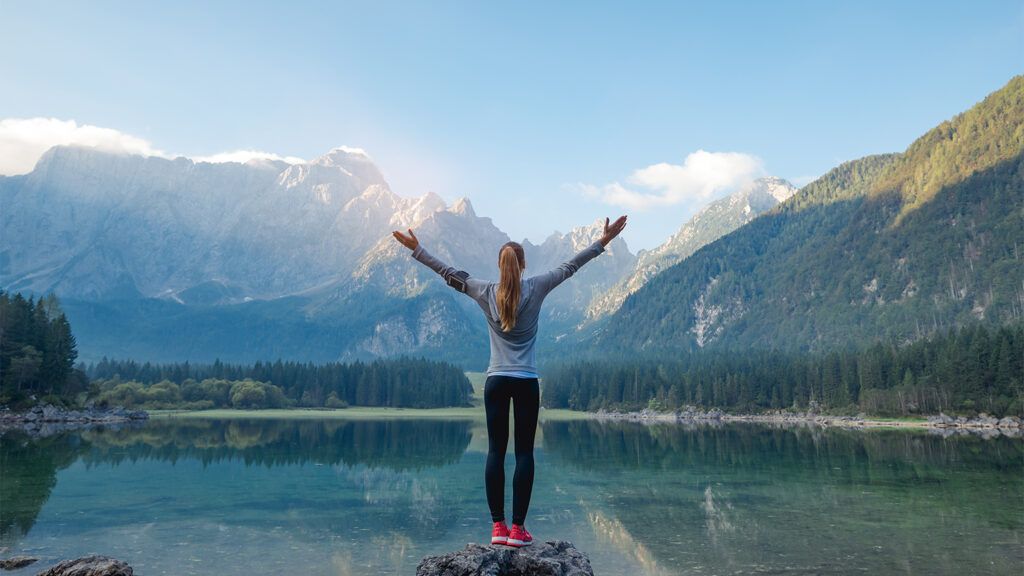 A woman stands at the edge of a mountain lake