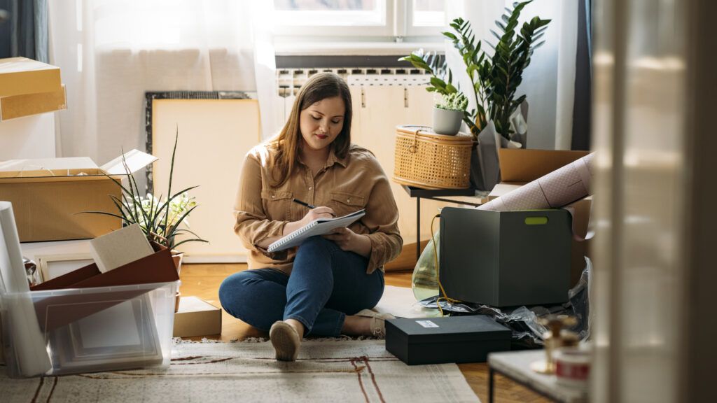 A woman sitting on the floor organizing her home and writing in a journal for her new year habit