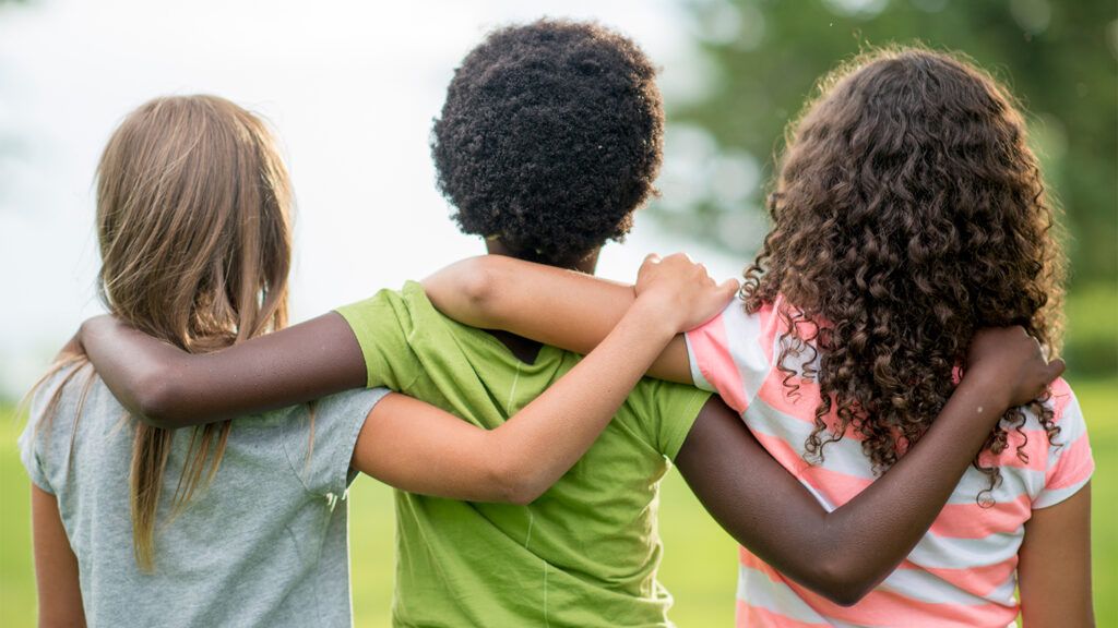 Three children stand, arms draped over one another's shoulders