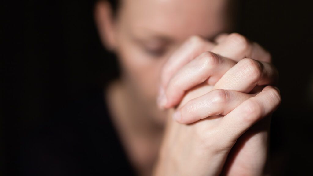 A woman clasps her hands in prayer