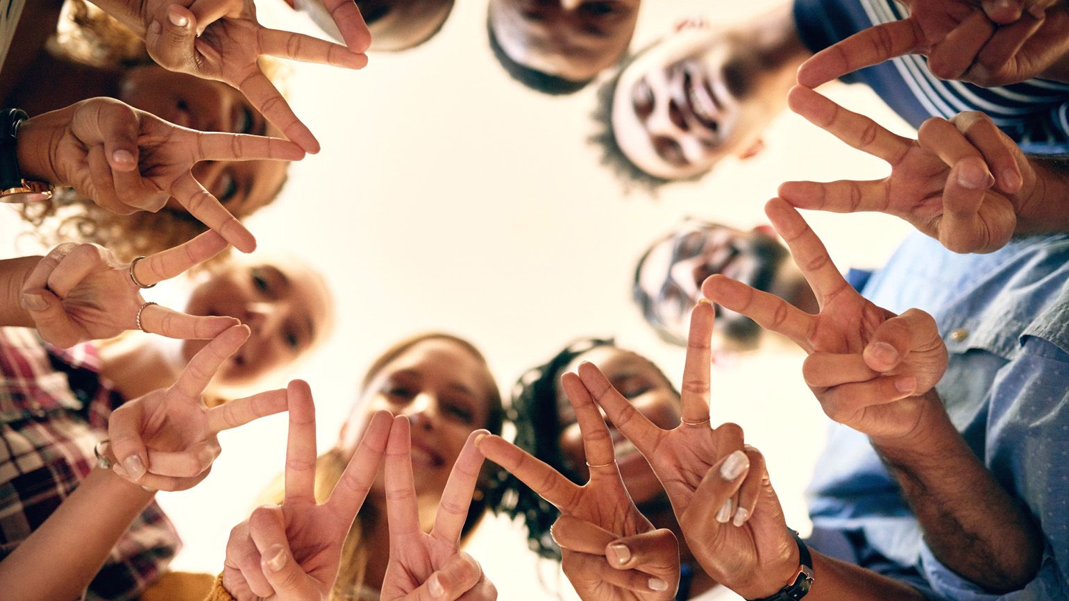 A diverse group of people in a circle holding up peace signs.