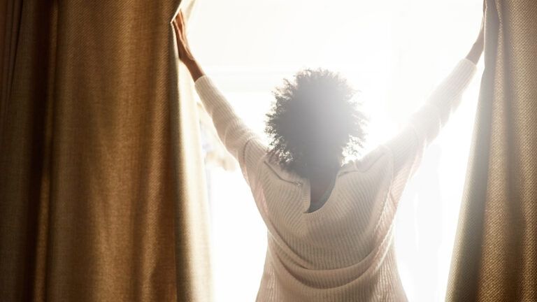 Woman opens the curtains to the greet the morning sun