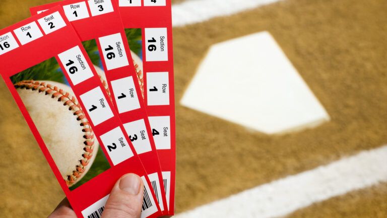 A Hand holding three baseball ticket stubs at home plate with the chalk lines of the batter's box