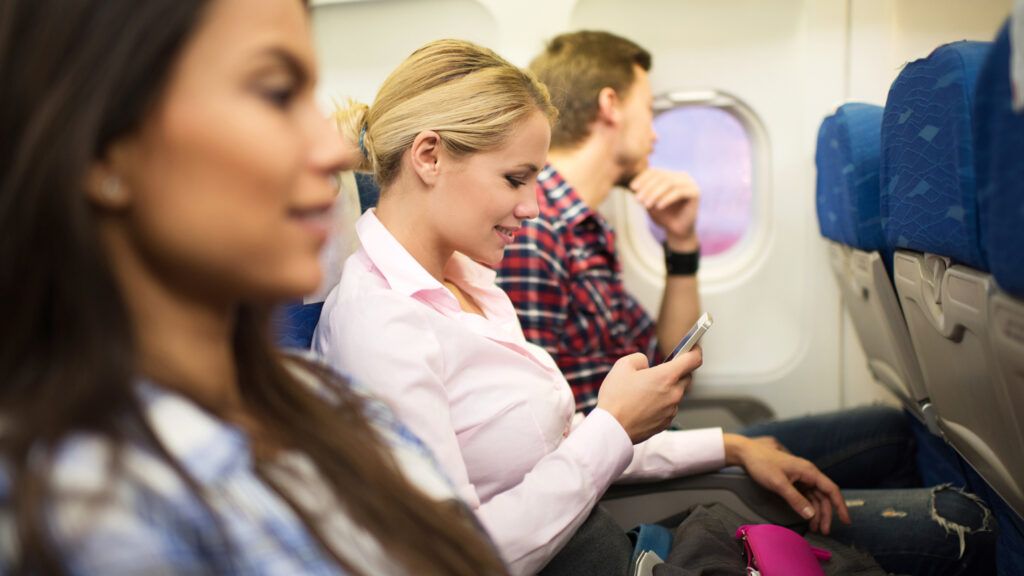 An airplane passenger smiles at her phone.