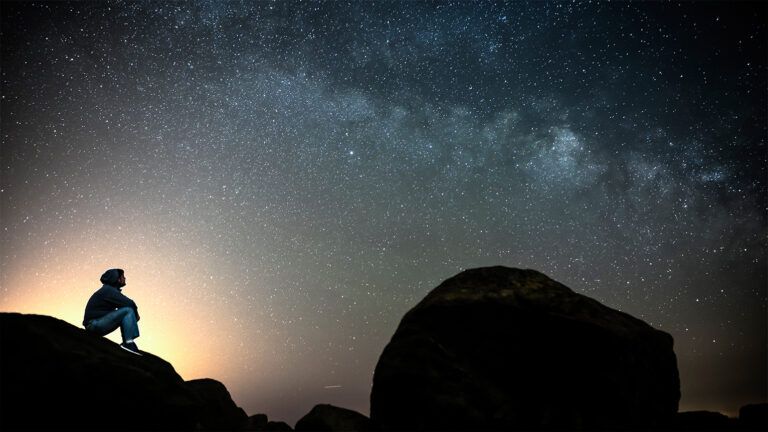 A boy sits on a hillside, gazing up at the stars