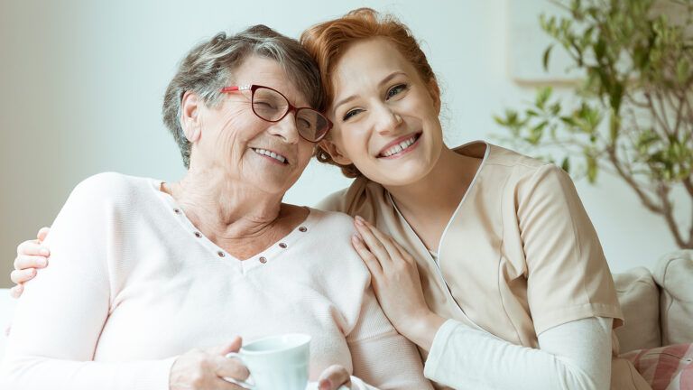 A smiling nurse gives her senior patient a hug