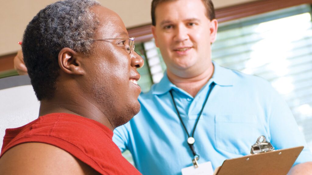 A man going through the rehabilitation program while a aide looks on to help.