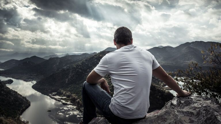 A man gazes out at sunbeams shining down on mountains