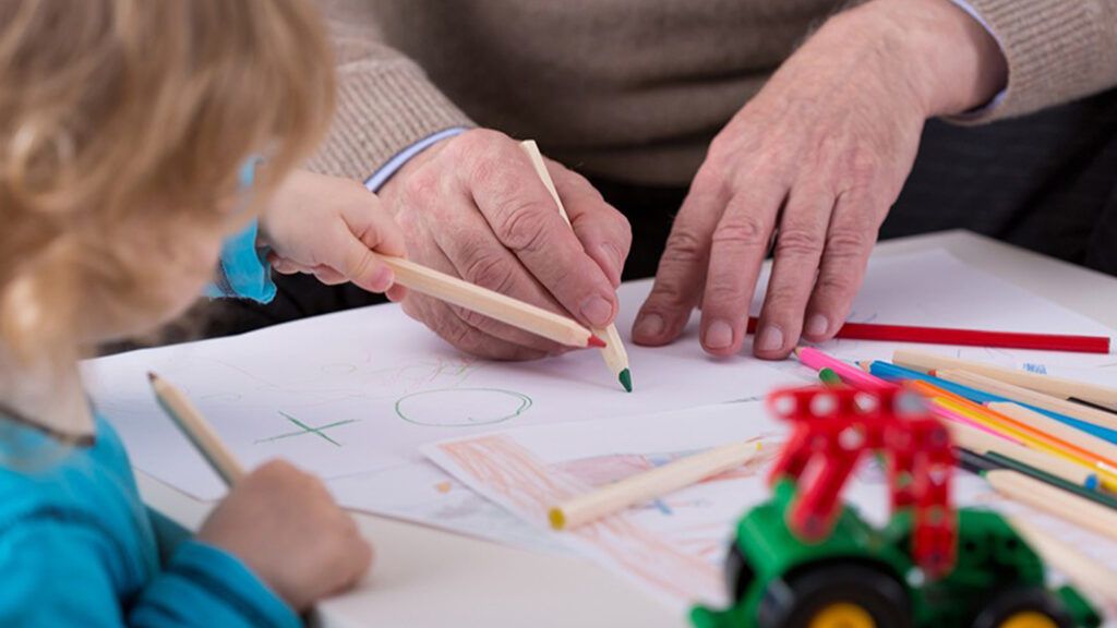 A grandfather drawing with his grandchild using colored pencils.