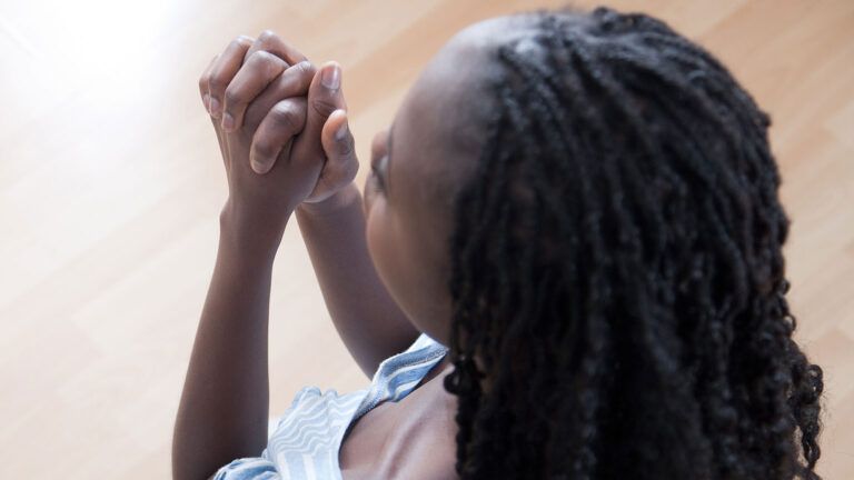 A young woman clasps her hands in prayer