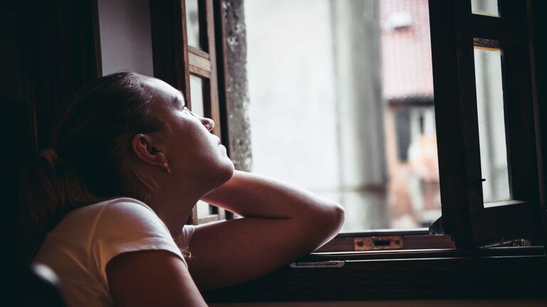 A woman looks upward out an open window