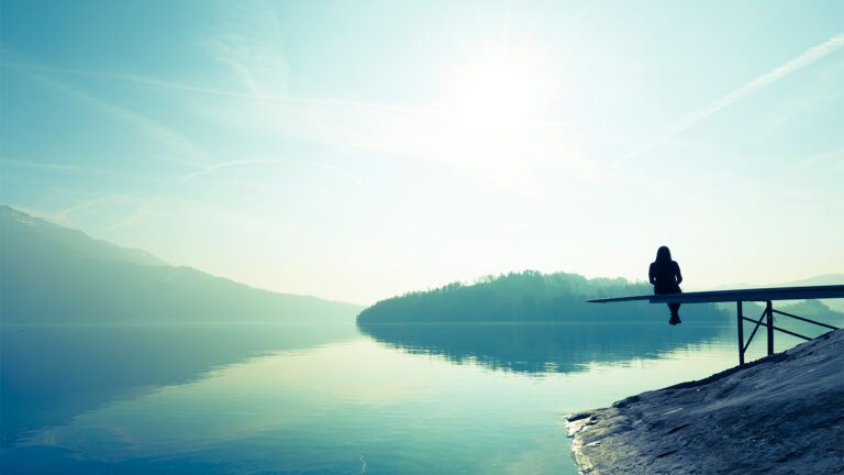 A woman sits on a pier above misty lake