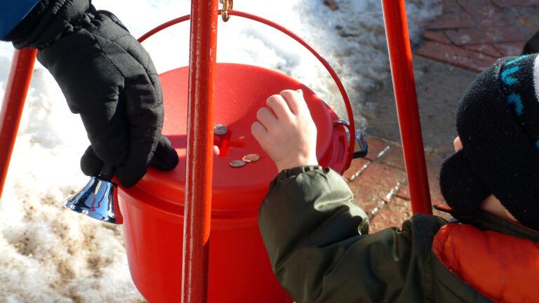 A young child drops coins in Christmas charity kettle