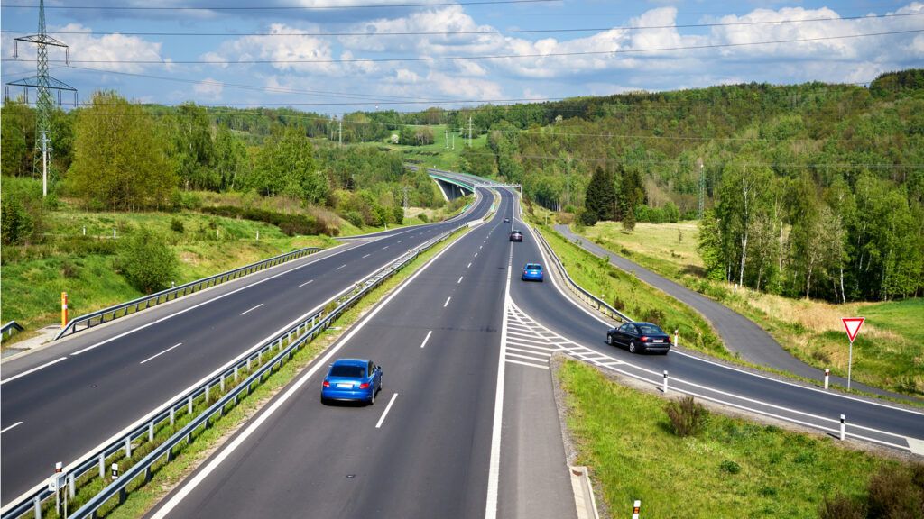 Various cars entering a highway lined with lush forests.