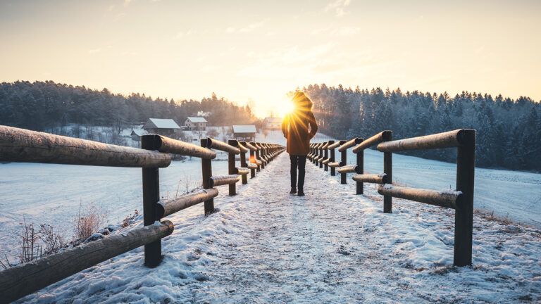 A woman gazes at the sunrise from a snow-covered country lane