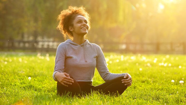 A smiling woman sits cross-legged in a sun-drenched meadow