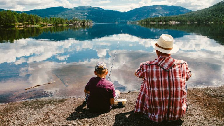 A father and son fish off a pier on a mountain lake