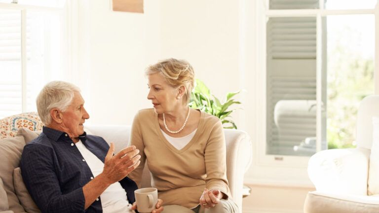 A senior couple having a chat and coffee break on their sofa at home.