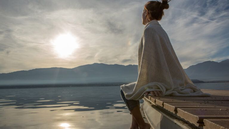 A woman sitting on the dock in deep reflection as the sun rises.