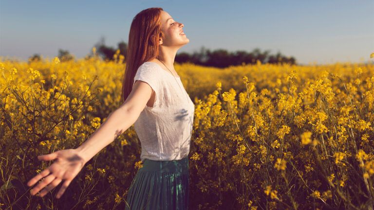 A woman stands, arms outstretched, in the sunlight