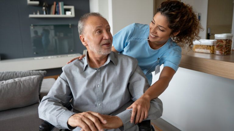 An in-home caregiver helping an elderly man in a wheelchair.