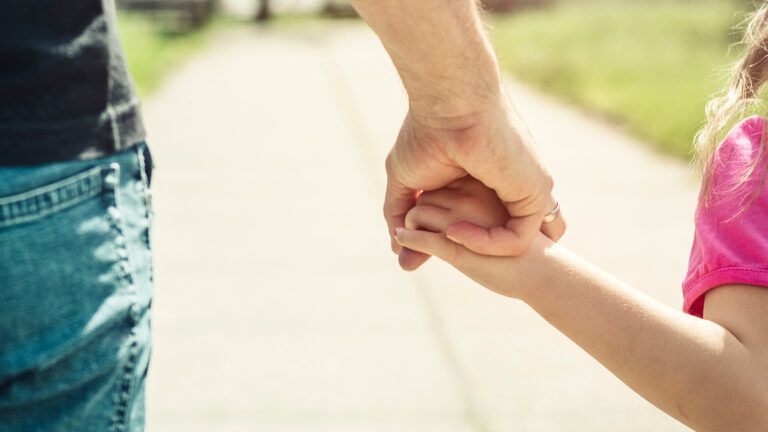 A fauther and young daughter hold hands