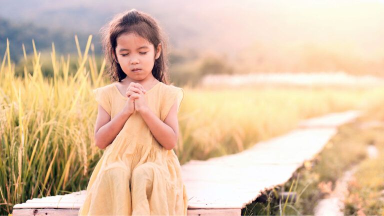 A young girl bows her head in prayer