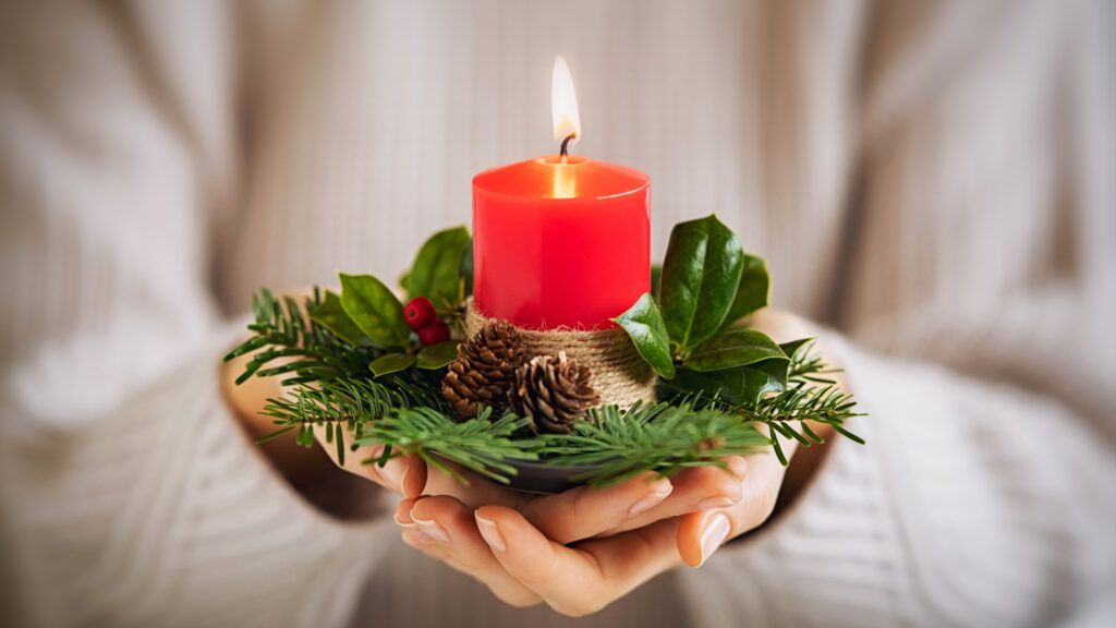 Woman in white sweater holding a candle saying an Advent prayer