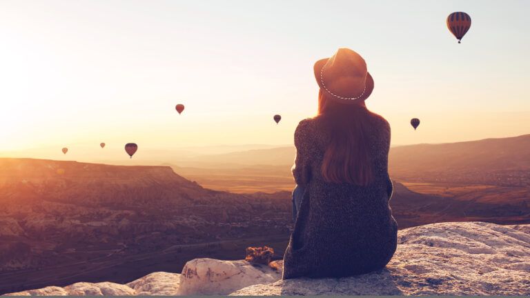 A woman sitting on a cliff at sunrise thinking about new years planners and new years devotionals