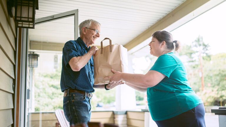 A young woman gives groaceries to a senior neighbor