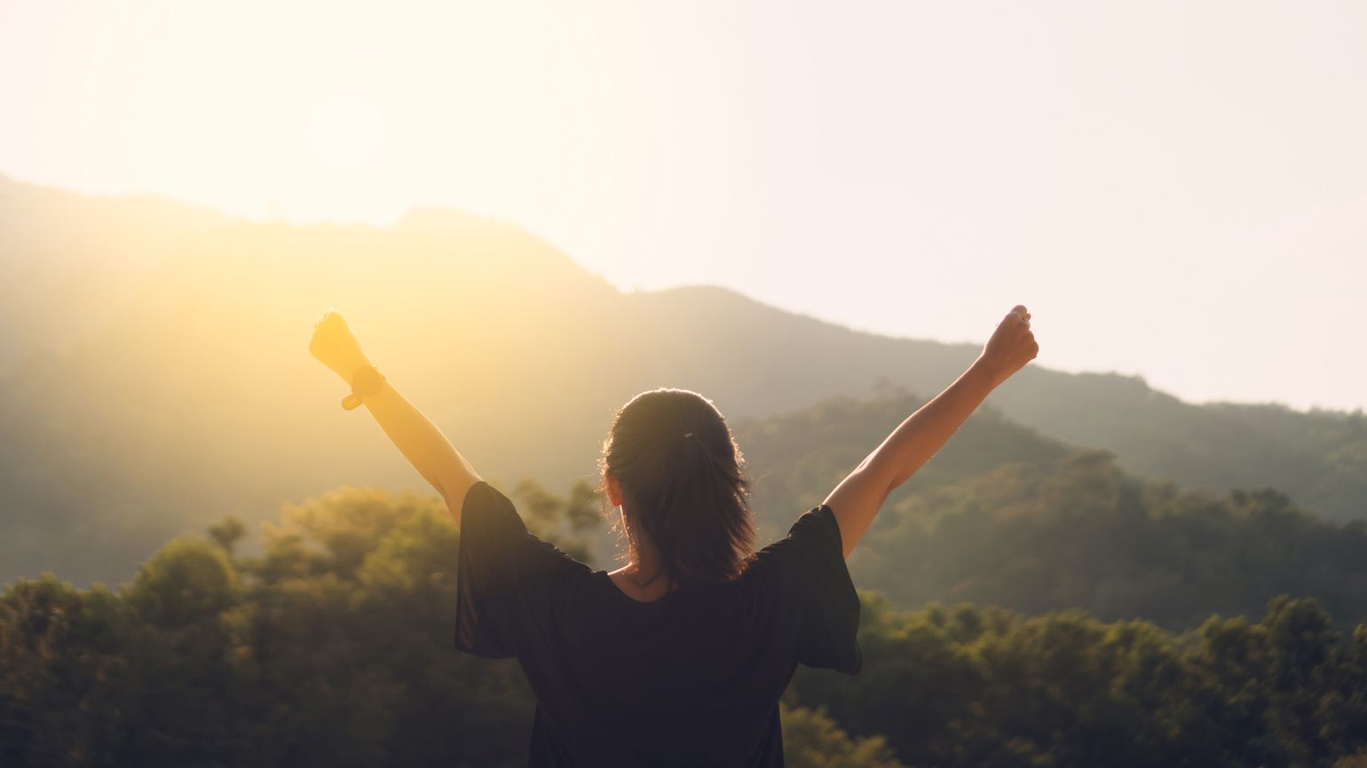 Woman with raised hands on mountain top; Getty Images