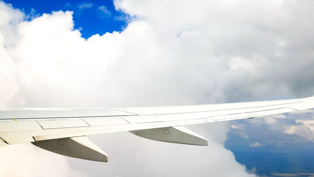 A view through an airplane window at the wing and the puffy clouds beyond