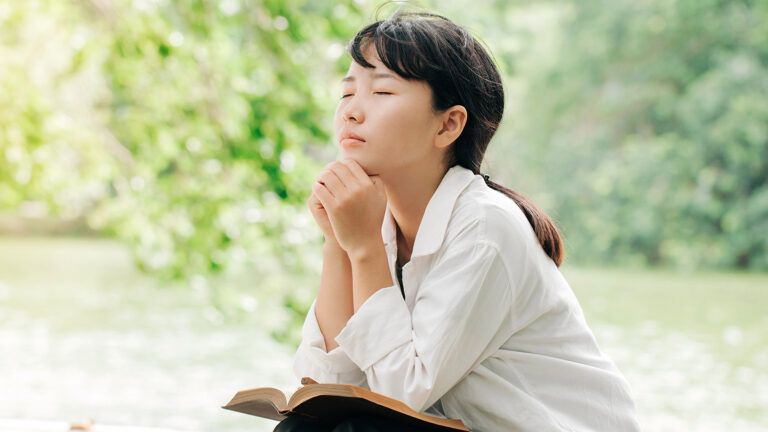 A woman kneels in prayer outdoors